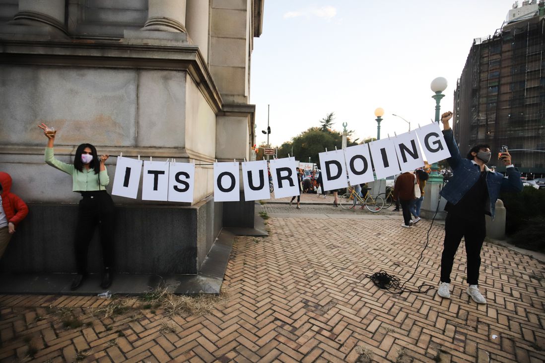 two people holding "it's our doing" sign